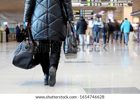 Woman with hand luggage walking inside airport building on passengers background. Concept of traveler before flight