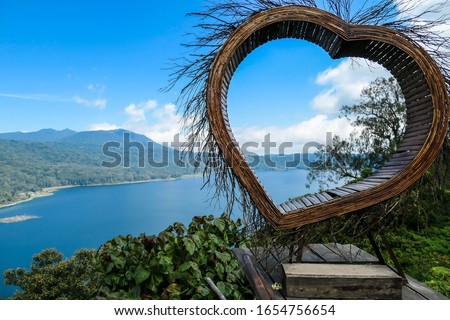 A wooden heart shaped seat with The Twin Lake in the background, Bali, Indonesia. The seat is high above the lake, made especially to take panoramic pictures. She is having fun. Touristic attraction