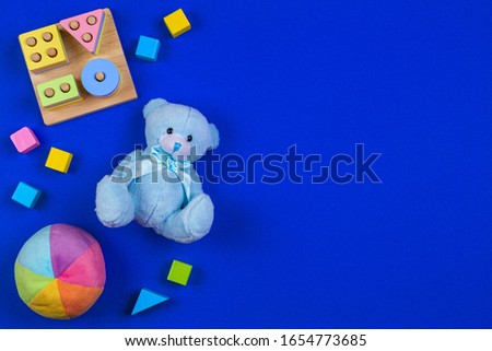 Baby kids toys background. Blue teddy bear, colorful wood blocks, shape color recognition puzzle stacker on navy blue background. Top view