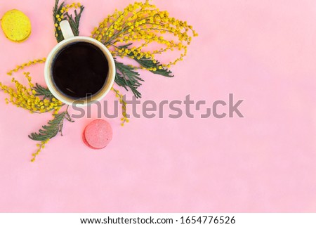Cup coffee, twigs with yellow flowers mimosa and colorful macaron cookie on a pink background with space for text. Spring decoration, composition. Top view, flat lay