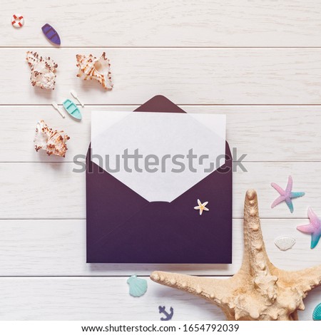 Vacation or travel planning concept. An empty sheet of paper is in a black envelope. Nearby are miniature figures of boats, starfish, seashells, helm and lifebuoy. Light wooden background. Flat lay.