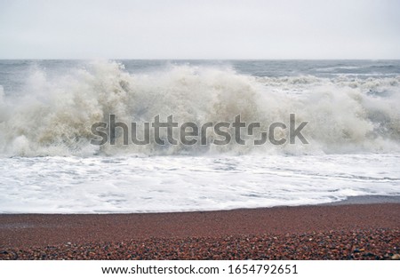 A sea scene of a very rough day at sea with the waves crashing onto the pebble beach creating sea spray, bubbles and foam 