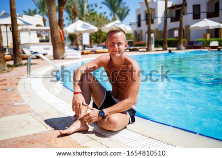 Guy in shorts bathes in the pool under the bright sun