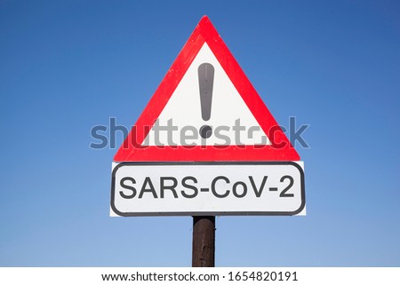 road warning triangle with black  exclamation point and red frame on  a wooden mast in front of a blue sky. A second rectangular sign warns in english about  SARS-COV-2 virus epidemic or pandemic Royalty-Free Stock Photo #1654820191