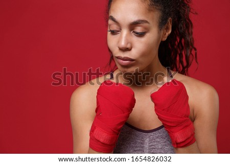Beautiful young african american sports fitness boxer woman in sportswear working out isolated on red wall background. Sport exercises healthy lifestyle concept. Wearing sports bandages on her hands