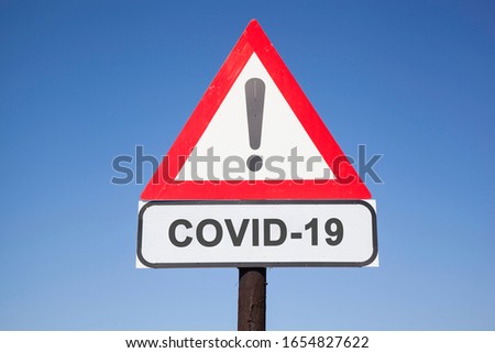 White road warning triangle with black  exclamation point and red frame on  a wooden mast in front of a blue sky. A second rectangular sign warns about  SARS-COV-2 virus epidemic or pandemic Royalty-Free Stock Photo #1654827622