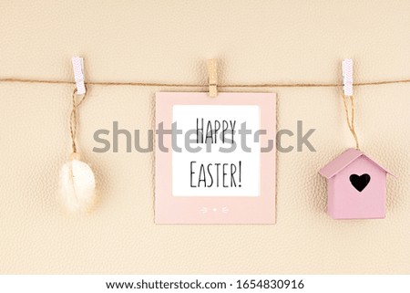 Easter greeting card hanging on the string with cute easter accessories over beige neutral background