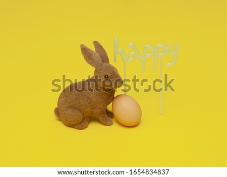 Brown Easter Bunny with an egg and a Happy sign on a yellow background. Minimal concept.