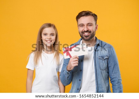 Smiling bearded man in casual clothes have fun with cute child baby girl. Father little kid daughter isolated on yellow background. Love family day parenthood childhood concept. Hold gift certificate