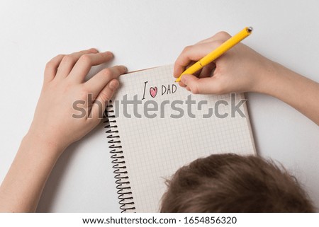 Child writes notice in notebook I love dad. White background Top view. Father's day concept.
