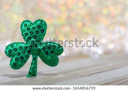 Green sequin shamrock for St. Patricks Day on wooden board soft warm color bokeh room for text