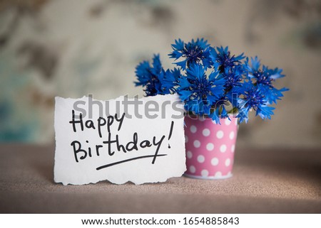 Happy birthday card with greeting words and blue cornflower flowers in pink vase