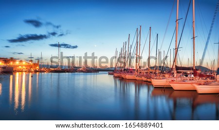 Night view of the Alghero Marina yacht port at the Gulf of Alghero with anchored sailboats. Location:  Alghero, Province of Sassari, Italy, Europe
