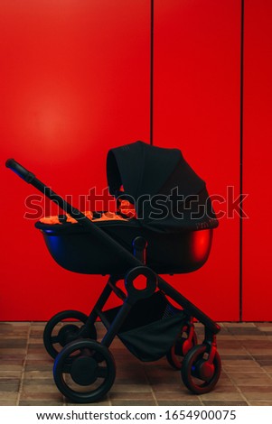 Modern black baby stroller on pavers with red background.