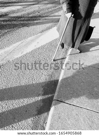 Legs of senior woman with stick crossing road at pedestrian crosswalk