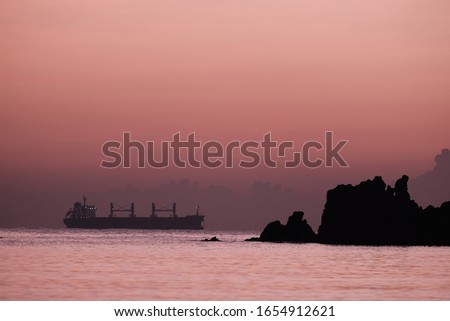 Blur of silhouette boat sailing the sea and rock island with orange pink shade in the morning sky
