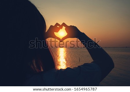women show heart shape by hand with the sunset on the beach