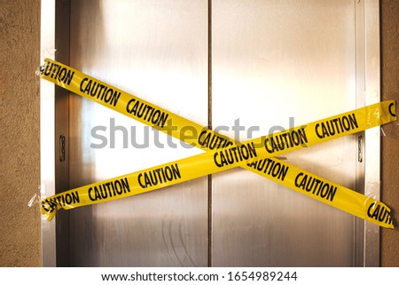 Broken elevator with warning sign,  yellow caution tape on stainless steel  elevator doors