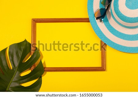 Top view on striped blue hat, sunglasses, monstera leaf and frame for vacation photos on yellow background. Concept of beach holiday, sea tour, warm sunny summer. Copy-paste