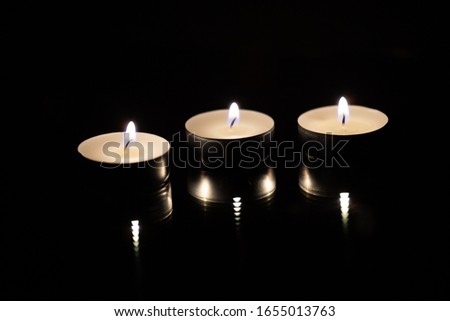 Three burning tea candles on a black background, close up.
