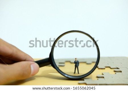 Business strategy conceptual photo - Miniature businessman standing behind magnifier glass in the middle of jigsaw puzzle 