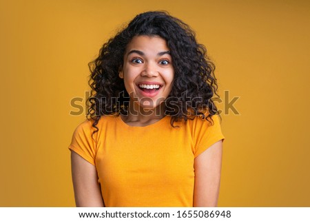 Studio shot close up portrait of casually dressed cute african american girl with funny astonished face expression. Emotional young mixed race woman with beautiful curly hair on bright background.