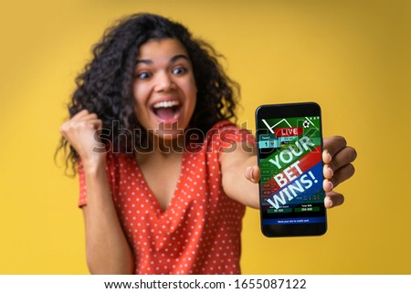 Girl being happy winning bet in online sport gambling application on her mobile phone clenchis her fist. Close up cropped shot. Focus is on hand. Isolated in bright yellow background. Royalty-Free Stock Photo #1655087122