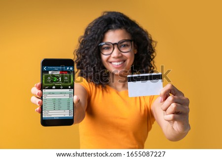 Cute african american girl watching football play online broadcast cheering for her favourite team and being happy about the score holding mobile phone and credit card. Her bet played. Isolated shot.