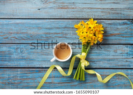 Morning cup of coffee and spring daffodil flowers on blue rustic background. Beautiful breakfast for Women day, Mother day. Top view.