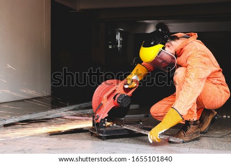 Asain male worker  in orange color mechanic jumpsuit using electric wheel grinding on steel . Sparks from the grinding wheel