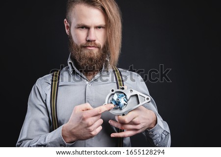 Studio portrait of a bearded stylish long-haired man in a shirt with suspenders. Holding car parts
