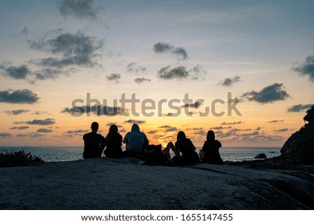 A group of young guys and girls meets dawn on a rock by the sea
