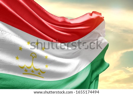 Tajikistan national flag cloth fabric waving on the sky with beautiful sun light.