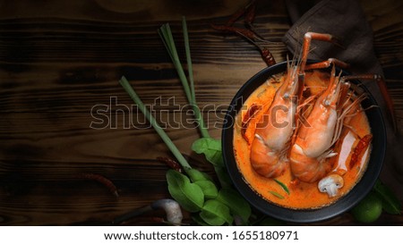 Top view of woman eating Tom yum goong, Thai traditional food with prawns, hot spicy soup , Thai herb ingredients and copy space on wooden table