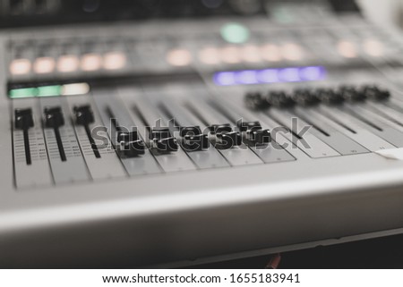 Abstract image of a music system, showing fader sliders and buttons. Lights can be seen turned on in the background in blur. Music system is in a retro silver colour and shows some nice depth of field
