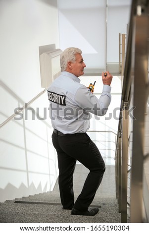 Professional security guard with flashlight on stairs indoors