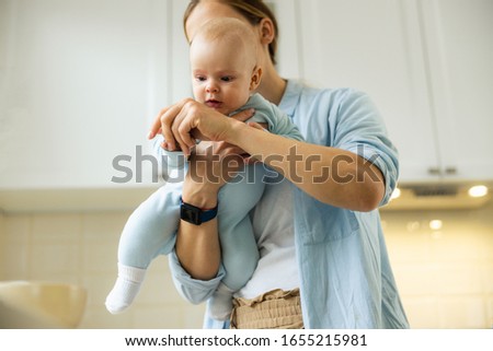 Happy woman holding her little kid while using smartphone for blog in the kitchen stock photo