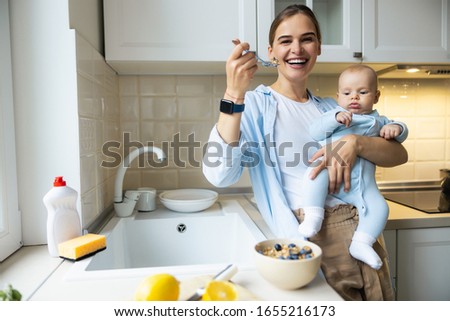 Smiling young woman enjoying breakfast while standing with her little child in the kitchen stock photo