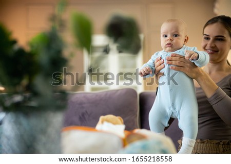 Happy beautiful young lady sitting on bed with newborn baby in arms stock photo
