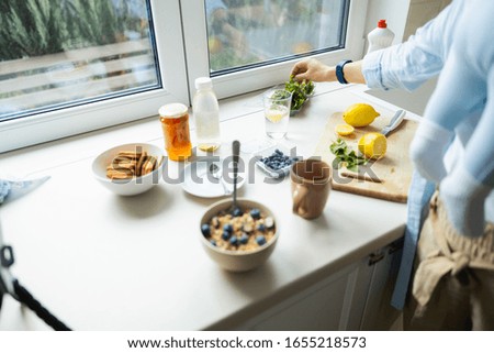 Lady holding baby while using smartphone for blog in the kitchen stock photo