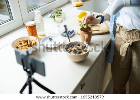 Young mom holding baby while using smartphone for blog in the kitchen stock photo