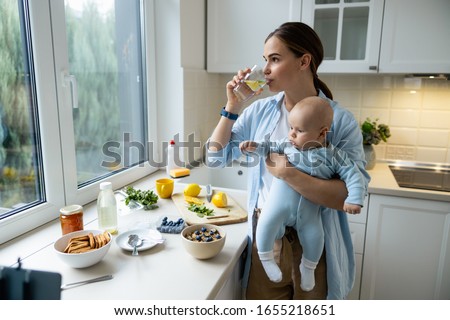 Young mom holding kid while drinking water at home stock photo