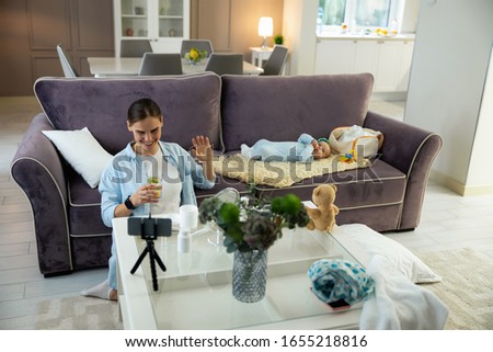 Happy pretty mom holding glass of water and using mobile phone for blog stock photo