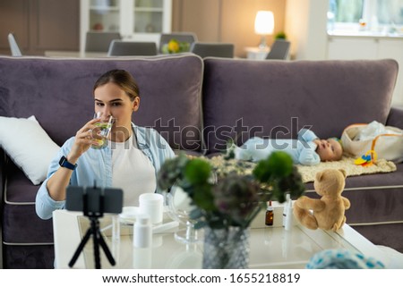 Happy young mother holding drinking water and using mobile phone for blog stock photo