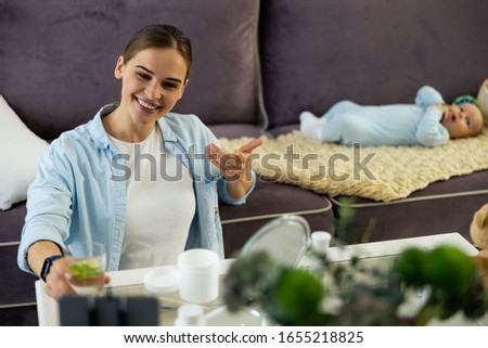 Happy pretty young mom holding glass of water and using smartphone for blog stock photo