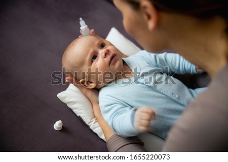 Close up of happy mother dripping drops in her baby nose in living room stock photo
