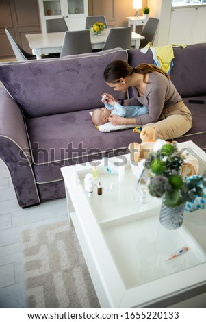 Top view of pretty mom dripping drops in baby nose while sitting on sofa stock photo