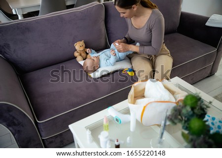 Top view of mom dripping drops in baby nose while sitting on sofa stock photo