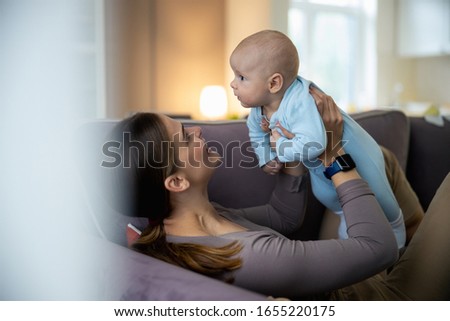 Happy beautiful young mother having fun with newborn baby while lying on sofa stock photo