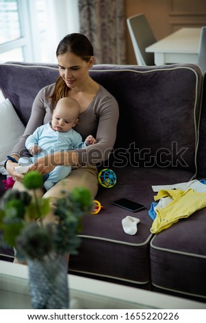 Happy pretty mom putting on socks to her child while sitting on sofa stock photo